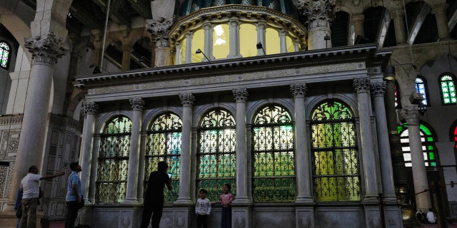 Visitors stand outside a domed shrine within a larger mosque