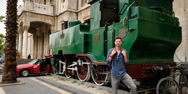 Leon McCarron poses next to a train car outside the Hejaz Railway Station in Damascus, Syria