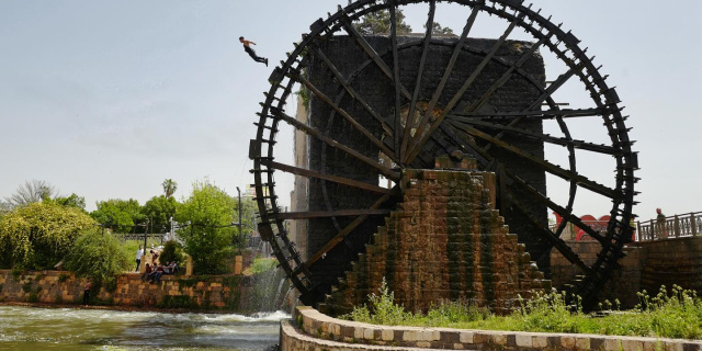 A teenager jumps from a medieval waterwheel into the Orontes River in Hama, Syria