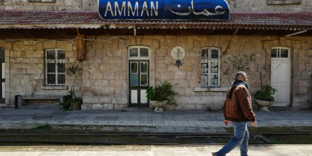 A man walks outside a train station with a sign reading "AMMAN" in English and Arabic