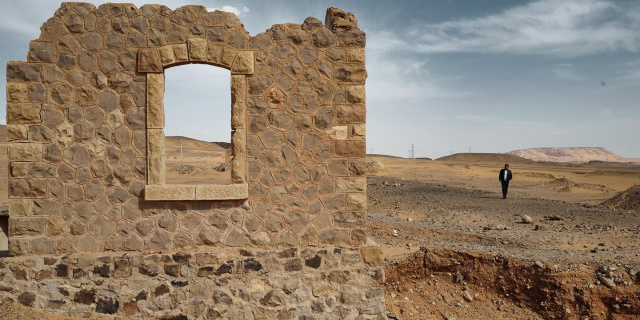 A partial building wall in the desert in Jordan with a man walking towards it